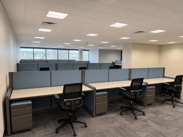 Rows of commercial open-plan systems cubicles with blue privacy panels and light maple desktops installed on a main office floor in Colorado Springs.