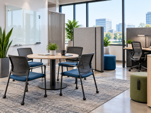 Technology office huddle space with round table, movable chairs, privacy screens, and nearby focus workstations