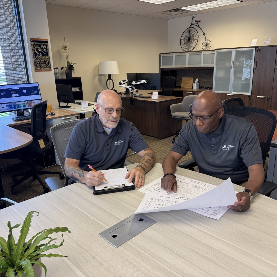 Two office furniture team members reviewing floor plans in a professional office showroom